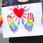 person celebrating lgbtq community in parade, holding a pride flag and a drawing